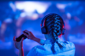 The gamer is playing a game against the background of a large screen or TV, new games are exclusive, a new era, rest time