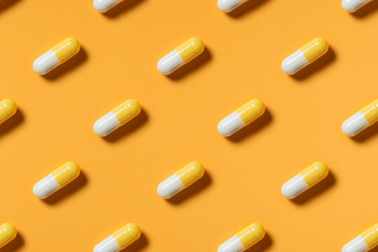 Yellow white pills or capsules lie in rows diagonal on orange background top view copy space pattern.