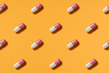 Pink and white pills or capsules lie in rows diagonal on orange background top view copy space pattern.