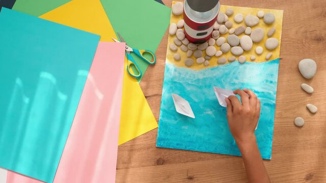Kid hands make a lighthouse for school project at home. Top down view to the table with colored paper and other supplies