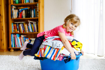 Little girl with a big basket of fresh clean laundry ready for ironing. Happy beautiful toddler and baby daughter helping mother with housework and clothes.