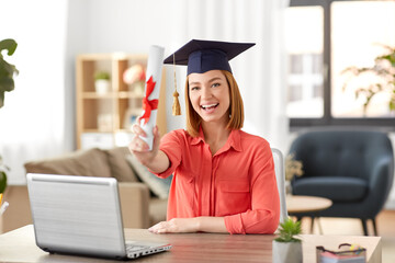 e-learning, education and people concept - happy smiling female graduate student in mortarboard with laptop computer and diploma at home - obrazy, fototapety, plakaty