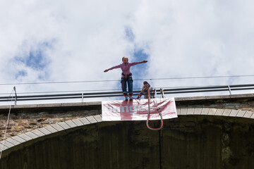 Senior lady jumping from a railway bridge watched by a young man - bungee instructor. Active senior woman. Bungee jumping.