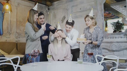 Excited pretty woman blowing birthday candles while dearest friends throwing surprise party