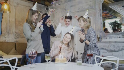 Excited pretty woman blowing birthday candles while dearest friends throwing surprise party