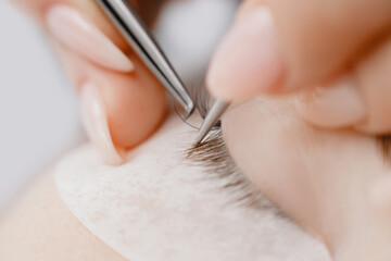 Obraz na płótnie Canvas Macro photo Eyelash extension procedure. Master tweezers fake long lashes beautiful female eyes