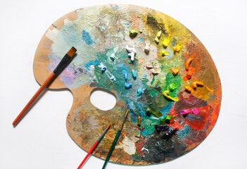 Colorful palette with oil paints and paint brushes on a white background
