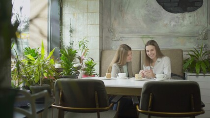 Two young women are looking at phone and smiling at cafe