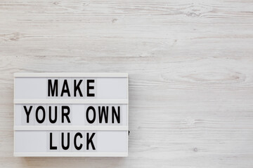 'Make your own luck' on a lightbox on a white wooden background, top view. Flat lay, from above, overhead. Space for text.