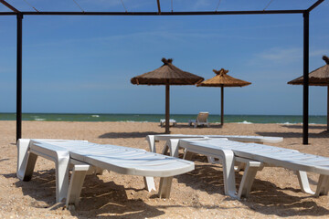 Empty beach view with white plastic chaise lounges deck chairs, awning and straw umbrellas parasol, resort and vacation concept