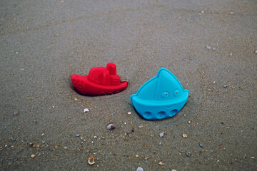 Two plastic bright, red and blue, sand toys molds in ship boat shape, play with kids in beach with wet sand, happy vacation