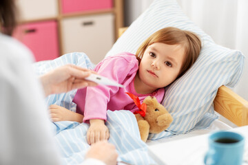 healthcare, medicine and people concept - close up of doctor with thermometer measuring temperature of little sick girl lying in bed at home