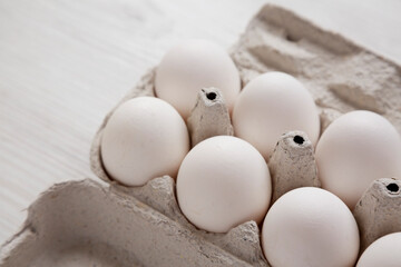 Uncooked Organic White Eggs in a paper box on a white wooden surface, side view. Copy space.