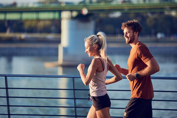 Obraz premium Modern woman and man jogging / exercising in urban surroundings near the river.