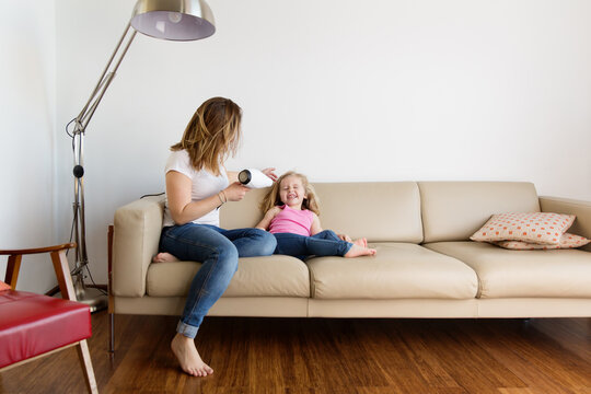 Mother drying daughter's hair on sofa at home