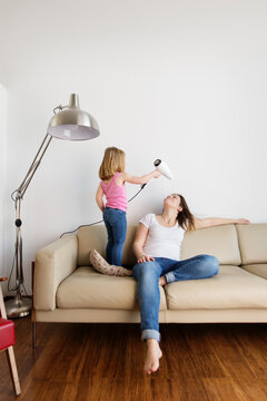Girl drying mother's hair on sofa at home