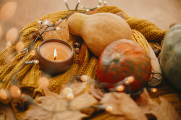 Pumpkins, autumn leaves, candle, warm lights and acorns, walnuts, berries on yellow knitted sweater on rustic wood. Hello fall. Cozy rustic autumn image. Happy Thanksgiving