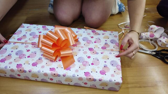 The girl packs a gift in a beautiful multi-colored paper and ties with an orange bow.