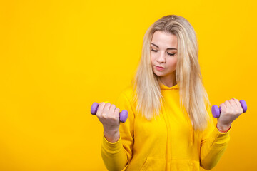 Serious beautiful young blonde woman in casual yellow sporty clothes doing exercises with small 0.5...