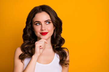 Closeup photo of pretty cunning curly lady red lipstick look curious empty space clever cruel idea hand on chin wear white casual tank-top isolated bright yellow color background