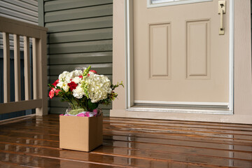 A bouquet of red white flowers in a carton box on a porch doorstep of a house. Surprise contactless...