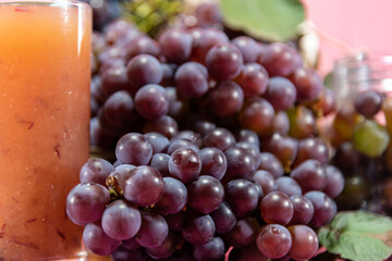 Glass of juice and bunches of grape on pink background