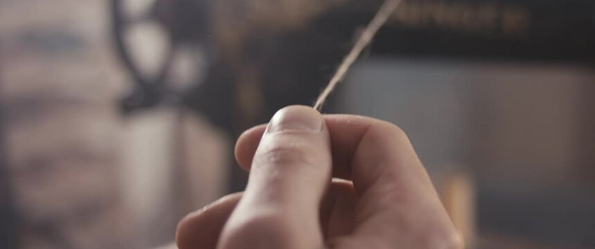 Traditional bespoke shoemaker wrap thread around finger hand on sewing machine in workshop unrecognizable extreme close up