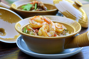 Casseroled shrimps with glass noodles in clay pot on wooden table