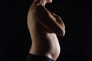 close up of pregnant woman naked on black background, six months;