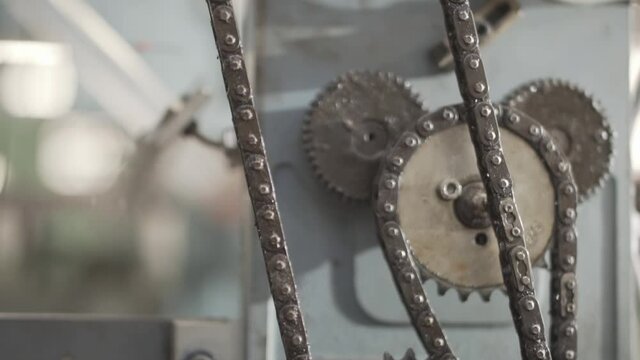 Metal gears slowly moving chain on ribbon making machinery - close up tilt up 