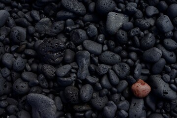 Una piedra roja o marrón en contraste con un fondo de piedras negras.