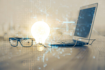 Computer on desktop in office with bulb icon hologram. Multi exposure. Concept of idea.