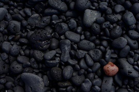 Una piedra roja o marr&oacute;n en contraste con un fondo de piedras negras.