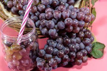Pot with grains and grape bunches on pink background