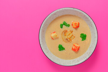 Creme soup with mushrooms served in a white bowl isolated on bright pink background. Copy space banner.