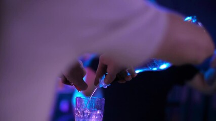 Bartender pouring transparent alcoholic drink  from a bottle into shot glasses. Closeup. Set of several glasses with cocktails. Barman pouring drinks into glasses for drinking. 