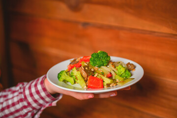 Waiter serving vegetable salad with juicy tomatoes, lettuce, radish, cucumber. Restaurant service.