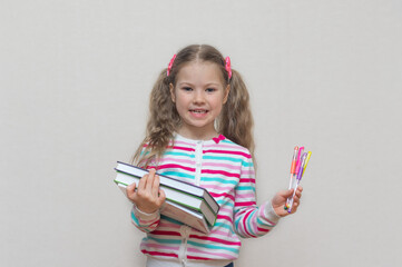 Back to school. Portrait of a blonde schoolgirl in a jacket with colored gel pens in her hands and books. The girl is smiling and looking at the camera. Light background. Education. copy place.