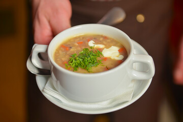 A waiter wearing plaid uniform serving a bowl of hot soup in a restaurant. Concept for a tasty and healthy meal.