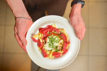 A servant is holding a plate with pasta, tomato sauce, parmesan and basil. Waiter at work. Restaurant service.