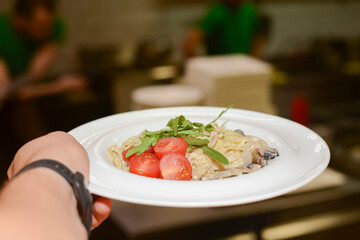 Traditional Italian pasta with tomato sauce and cherry tomatoes served in white plate in a hand of a waiter.