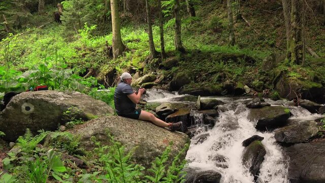 photographer hiker taking photos of waterfall and rocks with the camera, deep into mountains