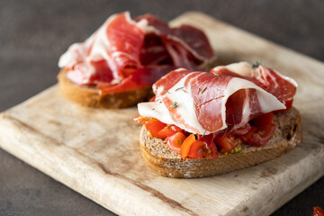 Two toasts with fresh tomatoes and cured ham. Delicious appetiser Italian prosciutto and Spanish...