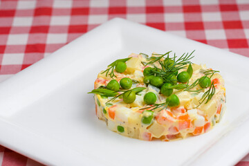 Vegetable salad with green peas and herbs and melted cheese served on a square white plate over red plaid tablecloth.