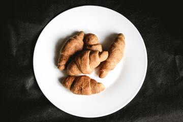 Croissants on a white plate on a black textile background. Fresh bakery