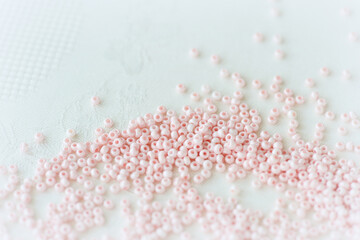 Pink seed beads scattered on the textile background close up. Handmade concept