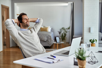 Happy businessman relaxing with eyes closed after working on laptop at home.