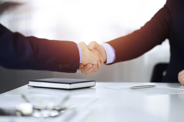 Business people shaking hands while sitting at the desk at meeting or negotiation, close-up. Group of unknown businessmen in a sunny modern office. Teamwork, partnership and handshake concept