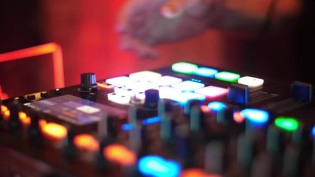 DJ hands in a nightclub colored lights. Color lights show in nightclub. Hands of DJ tweak various track controls on DJ mixer console at nightclub. Fingers touch buttons sliders. Sound beat maker. 