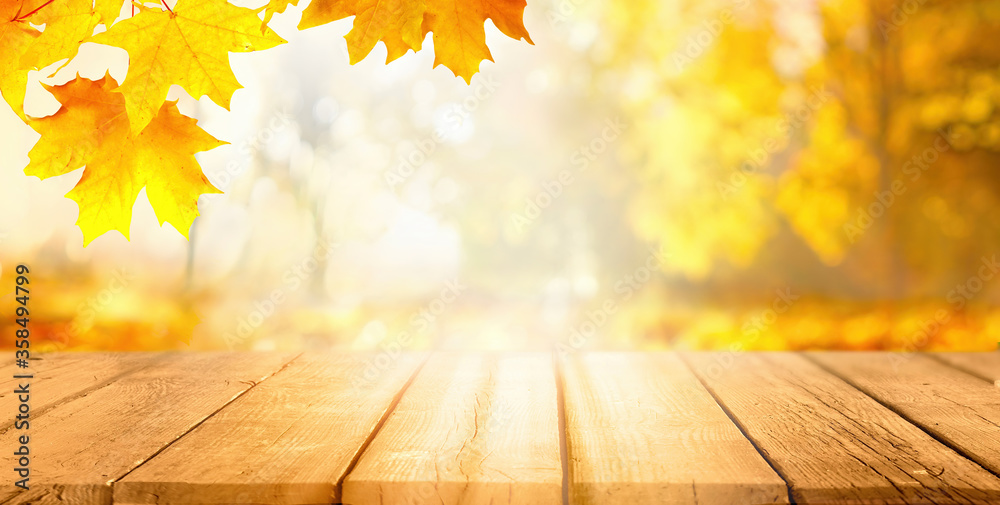 Poster Beautiful autumn background with orange gold maple leaves on background of sunlight with soft blurred bokeh and empty wooden table planks.